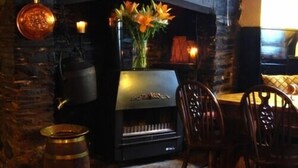 A cozy room with a fireplace, wooden chairs, and a table. - The Who'd Have Thought It Inn (Yelverton)