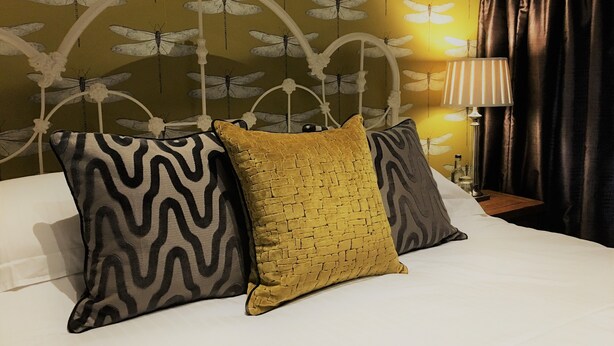 A bed with three pillows, a lamp, and a wall with a dragonfly pattern. - The Who'd Have Thought It Inn (Yelverton)