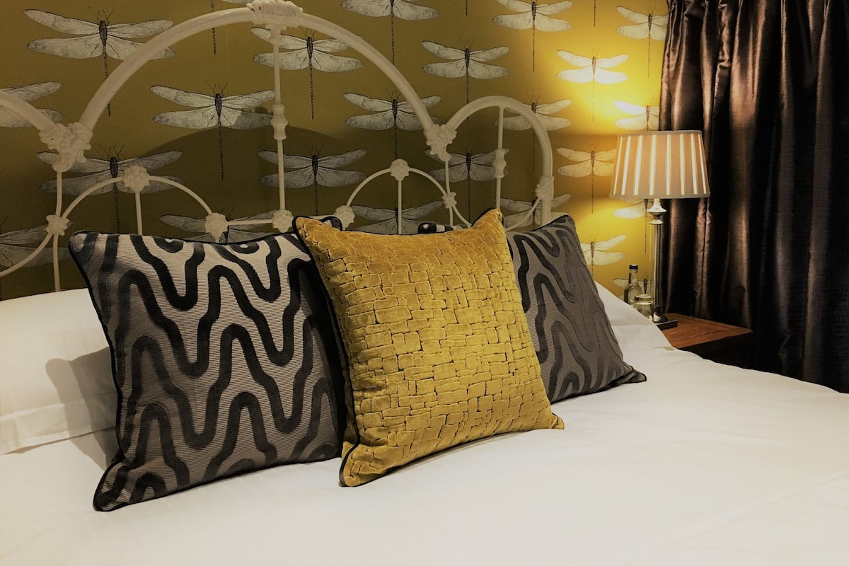 A bed with three pillows, a lamp, and a wall with a dragonfly pattern.