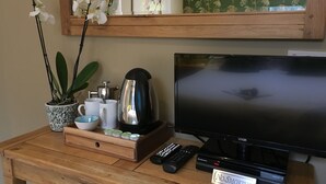 A wooden desk with a television, remote controls, a coffee maker, a mug, a cup, and a sign that says "No Smoking". - The Who'd Have Thought It Inn (Yelverton)