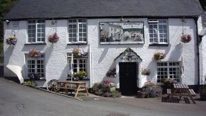 A white building with a black roof, a sign reading "16th Century Free House," and flower baskets on the windowsills. - The Who'd Have Thought It Inn (Yelverton)
