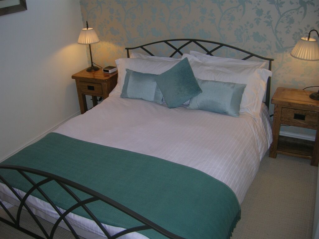 A neatly made bed with a green bedspread and pillows, two bedside tables with lamps, and floral wallpaper.