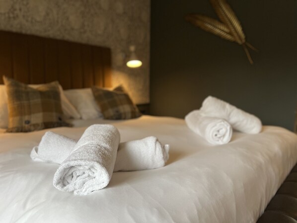 A neatly made bed with rolled white towels, a wooden headboard, and a wall with a textured pattern. - The Forresters Arms Kilburn (York)