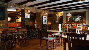 Un restaurante con mobiliario de madera, paredes de piedra y lámparas colgantes.