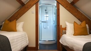 Un dormitorio con dos camas, cabina de ducha de vidrio, vigas de madera y techo inclinado.