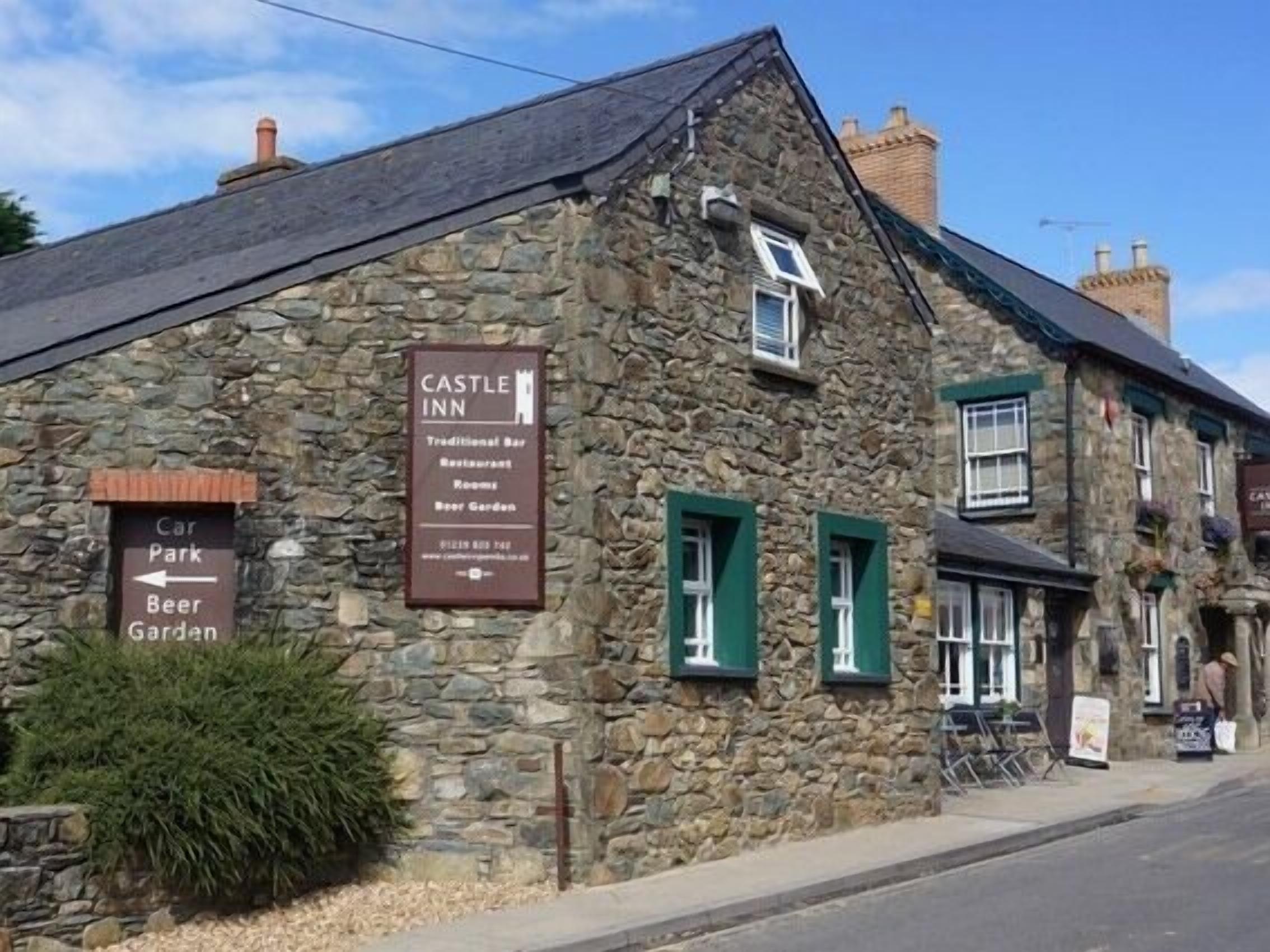 Un edificio de piedra con un cartel que indica que es el Castle Inn, ofreciendo un bar tradicional, restaurante, habitaciones y un jardín de cerveza.