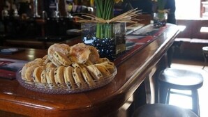Zona de bar con una vitrina que contiene pasteles y un jarrón con flores amarillas.