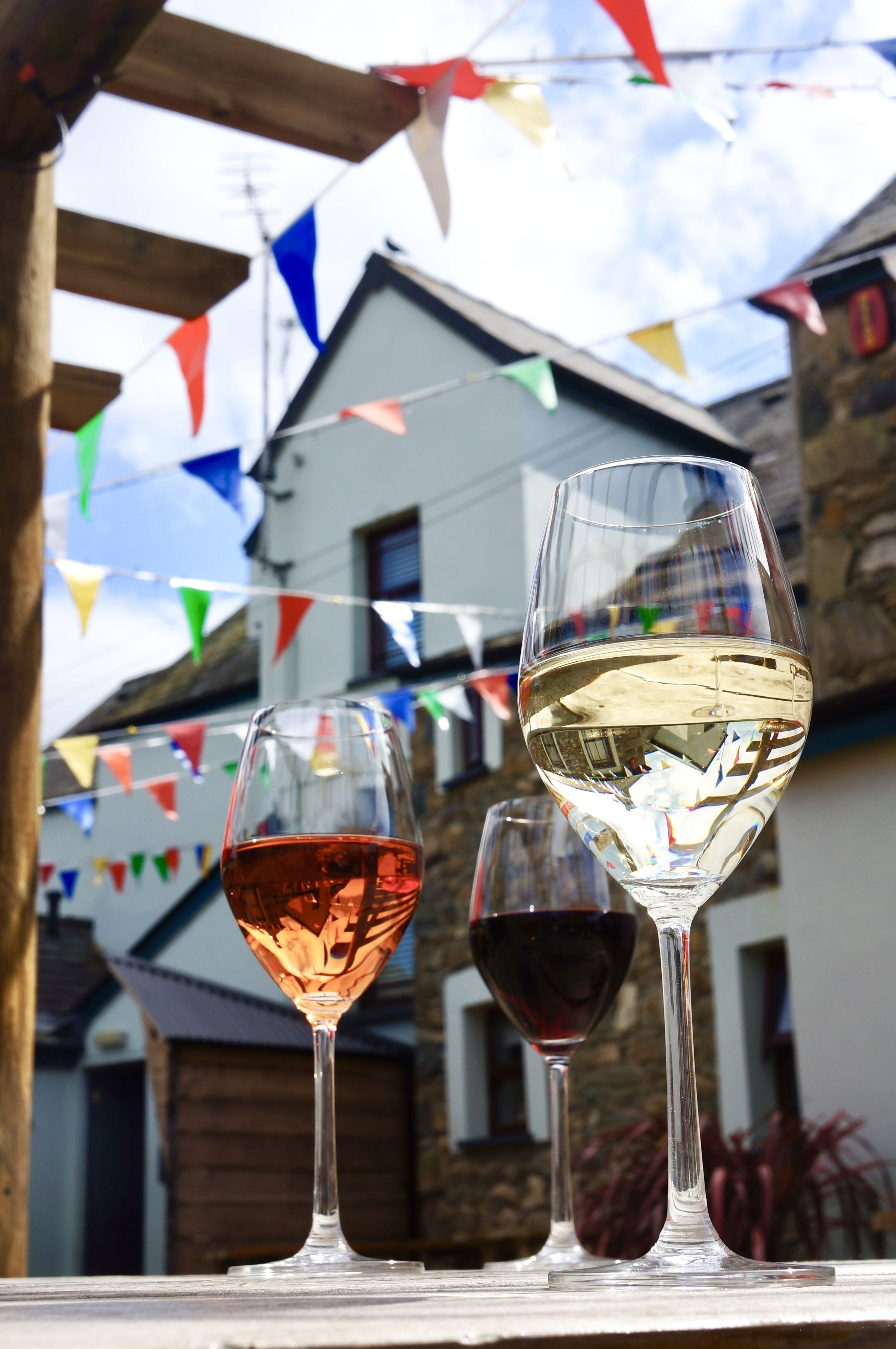 Two wine glasses on a table, one with red wine and one with white wine, under colorful triangular flags.