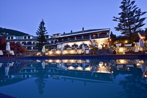 A large building with multiple balconies and outdoor seating areas, reflecting in a pool. - Hotel Prince Stafilos (Skopelos)