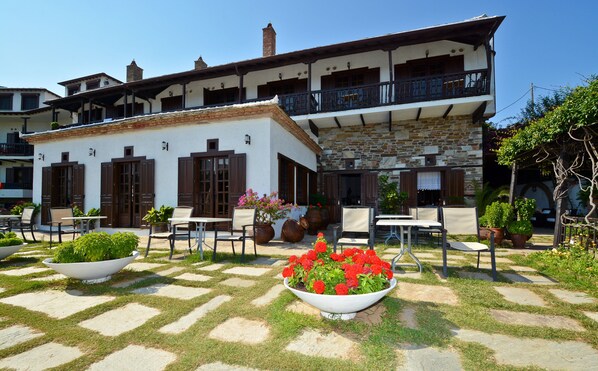 A two-story building with a balcony, outdoor seating area with tables and chairs, and potted plants. - Hotel Prince Stafilos (Skopelos)