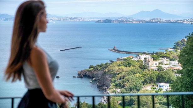 A coastal view with a lighthouse, rocky coastline, and buildings on a hillside. - Hotel Villa Ireos (Ischia)