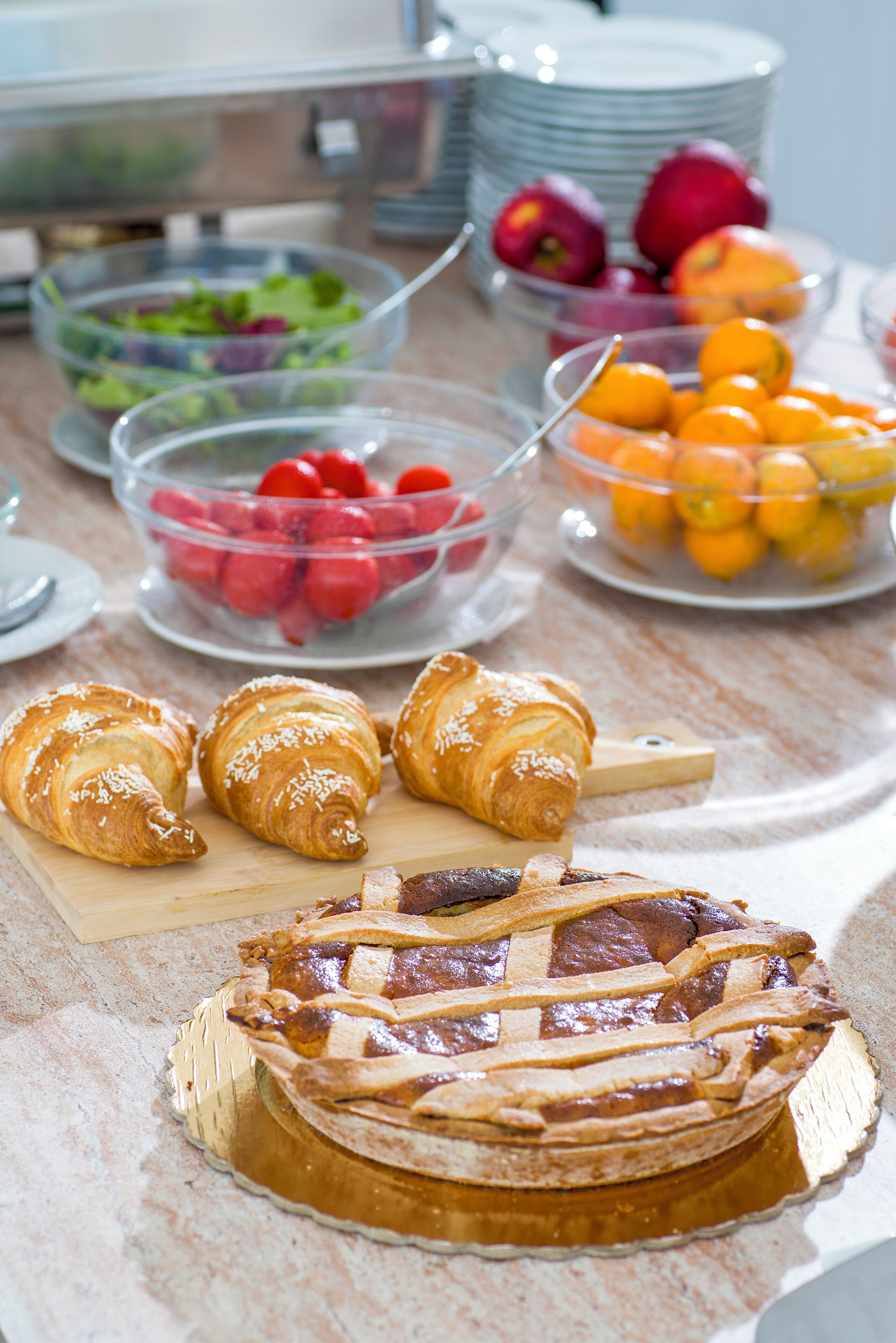 Un buffet de petit-déjeuner proposant une variété d’aliments, notamment des viennoiseries, des fruits et une tarte.