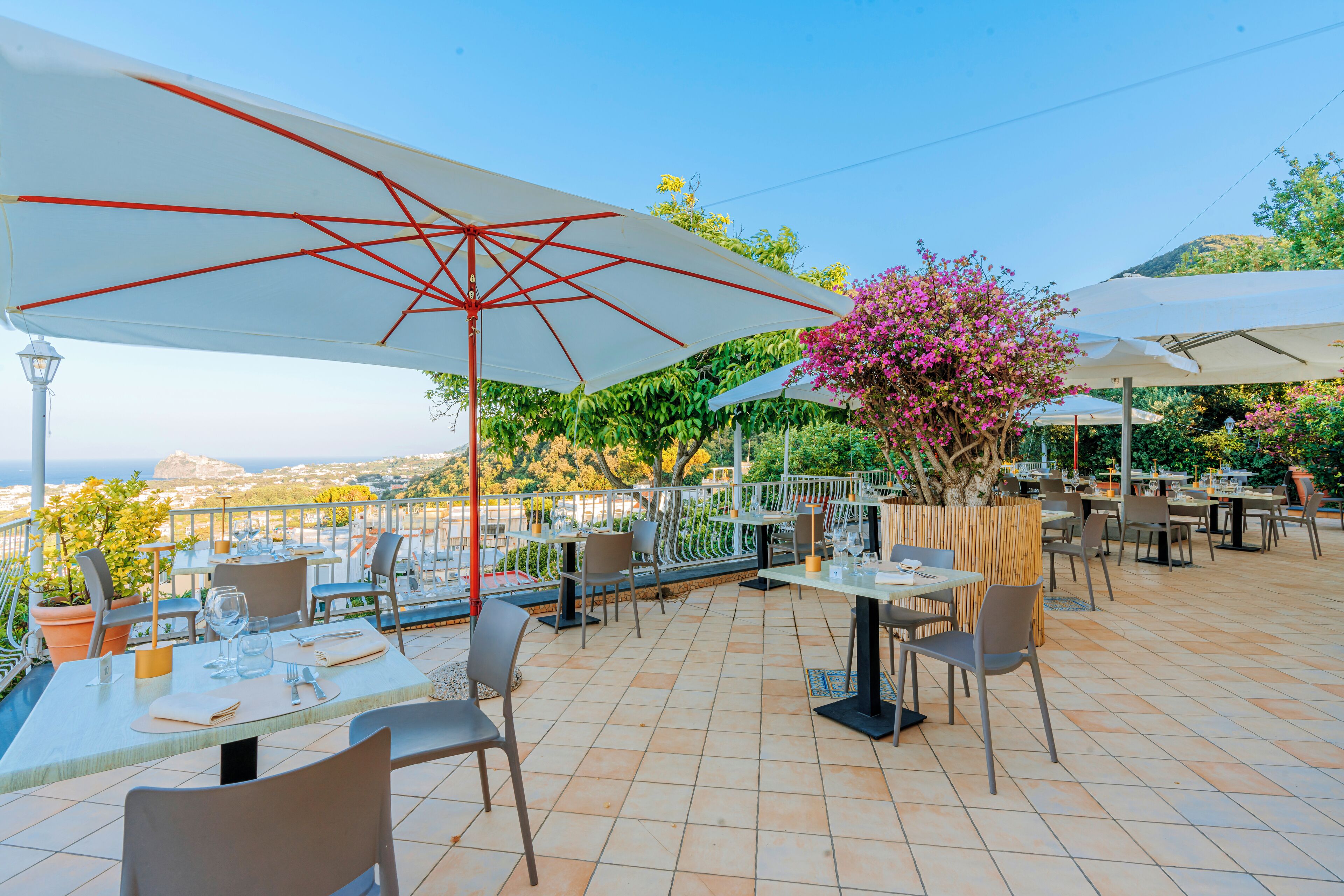 An outdoor dining area with tables and chairs, umbrellas, and a view of the city.