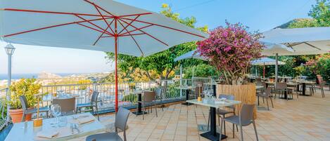 An outdoor dining area with tables and chairs, umbrellas, and a view of the city.