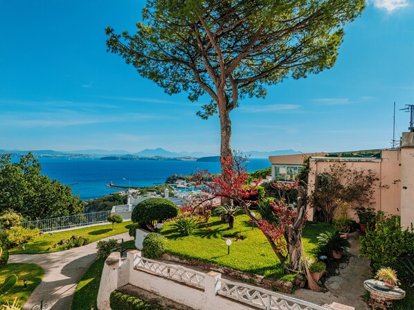 A coastal property with a view of the sea, a well-maintained garden, and a pathway leading to the entrance.