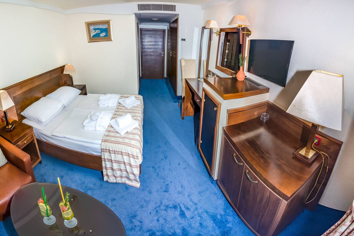 Une chambre d’hôtel avec un lit, un bureau, une chaise, une télévision et une petite table avec des boissons.
