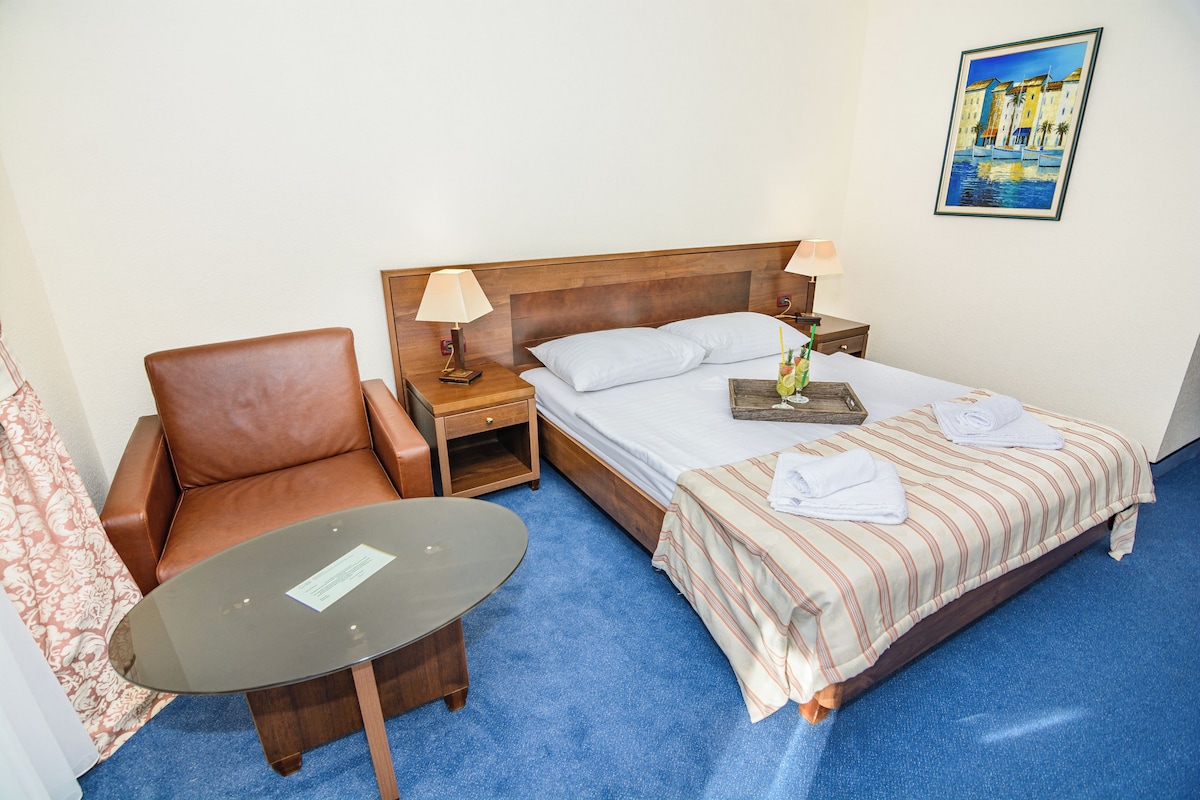 A hotel room with a bed, a chair, a small table, and a nightstand.