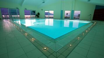 An indoor swimming pool with a view of the mountains through large windows.