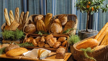 Variedad de panes y pasteles expuestos sobre una mesa de madera con cestas y una planta en maceta.
