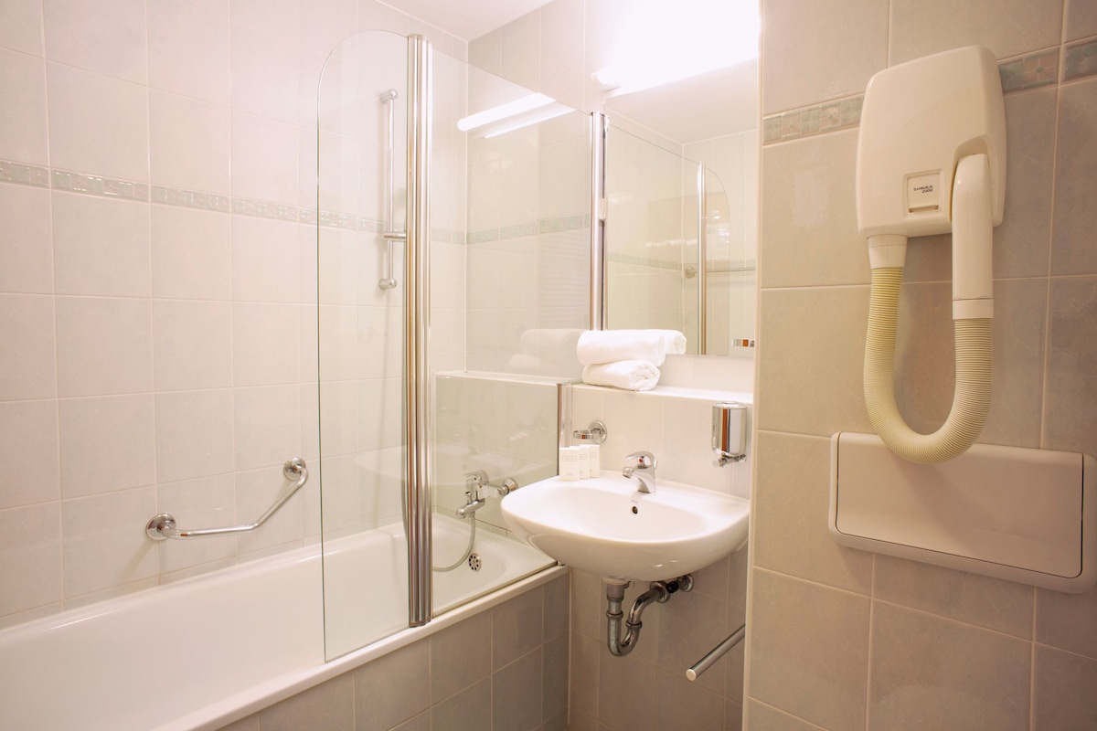 A modern bathroom with a glass shower enclosure, a white sink, and a built-in hairdryer.