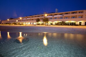 A hotel with multiple floors, a clear pool in the foreground, and well-lit surroundings. - Family Hotel Pagus (Pag)