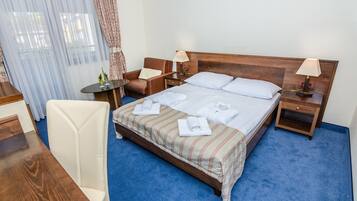 Una camera d'albergo con un letto grande, due comodini, una scrivania, una sedia e una finestra con tende.
