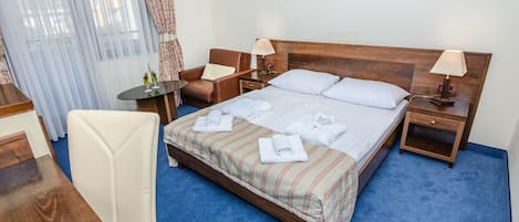 Hotelkamer met groot bed, twee nachtkastjes, een bureau, een stoel en een raam met gordijnen.
