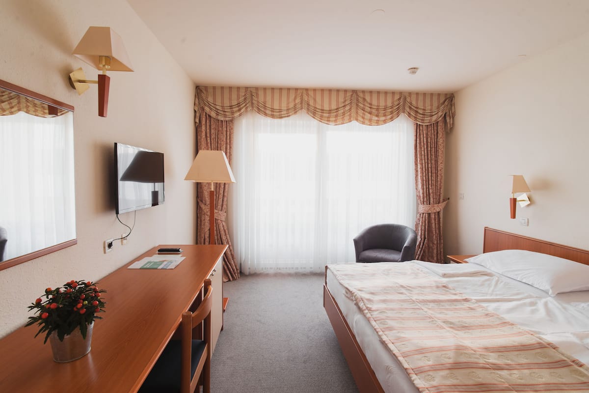 Une chambre d’hôtel avec un lit, un bureau, une chaise, une télévision et une fenêtre avec des rideaux.