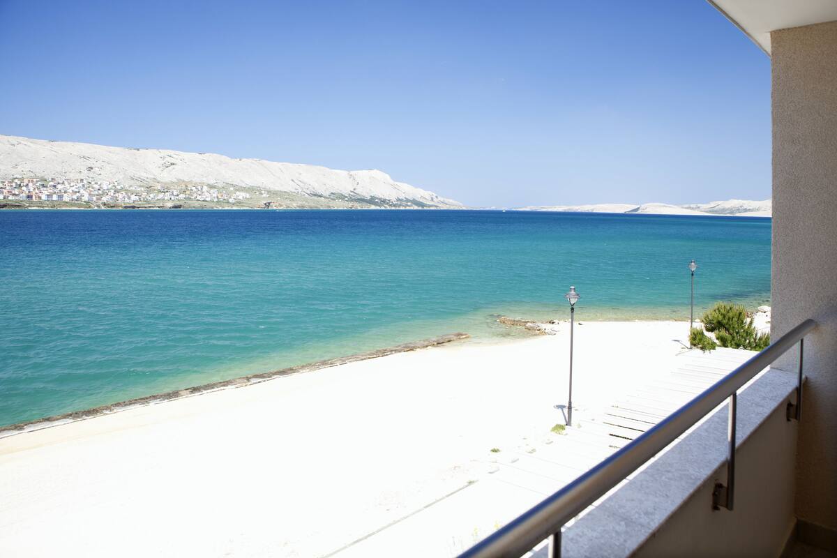 Un balcon donnant sur une plage et la mer, un lampadaire et une rambarde.
