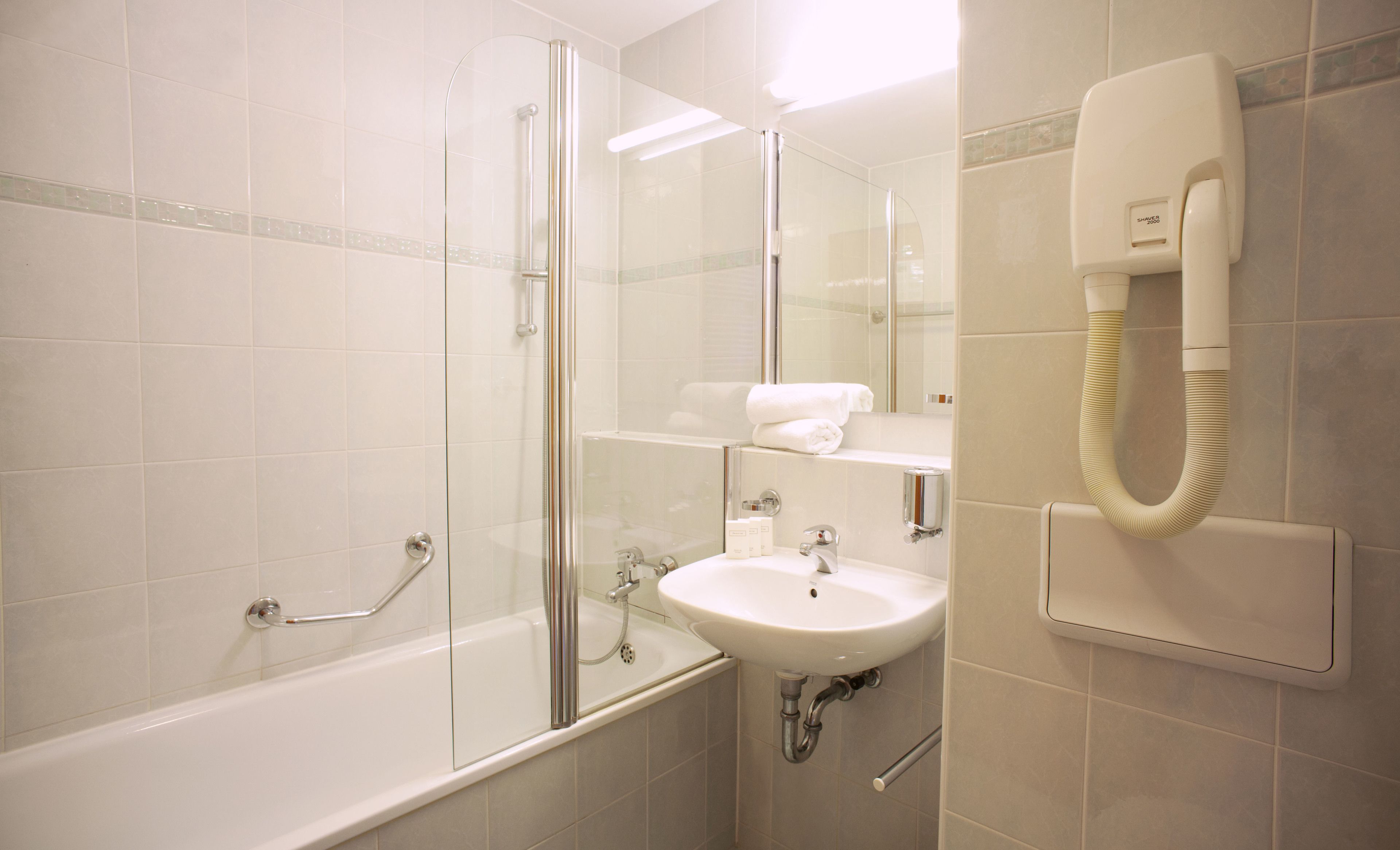 Ein modernes Badezimmer mit Duschkabine aus Glas, einem weißen Waschbecken und einem fest installierten Fön.