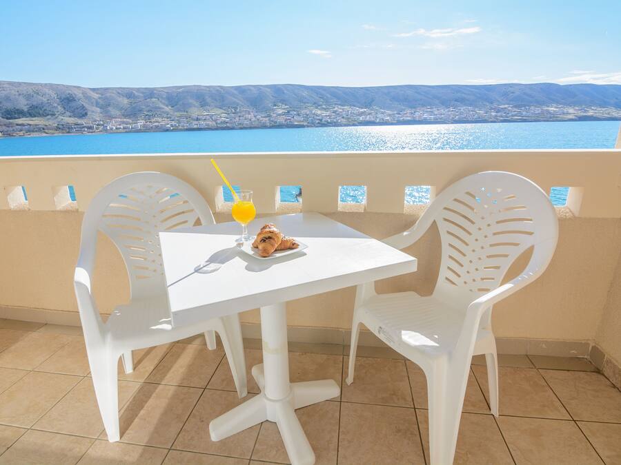 A balcony with a white table and chairs, a plate with food, and a glass of orange juice.