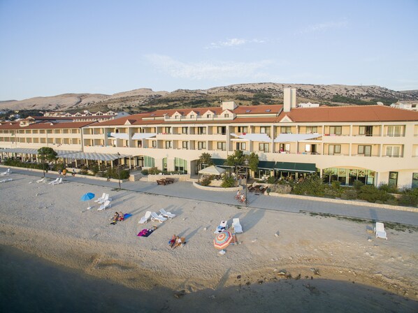 A hotel with multiple floors, outdoor seating areas, and a beach in the foreground. - Family Hotel Pagus (Pag)