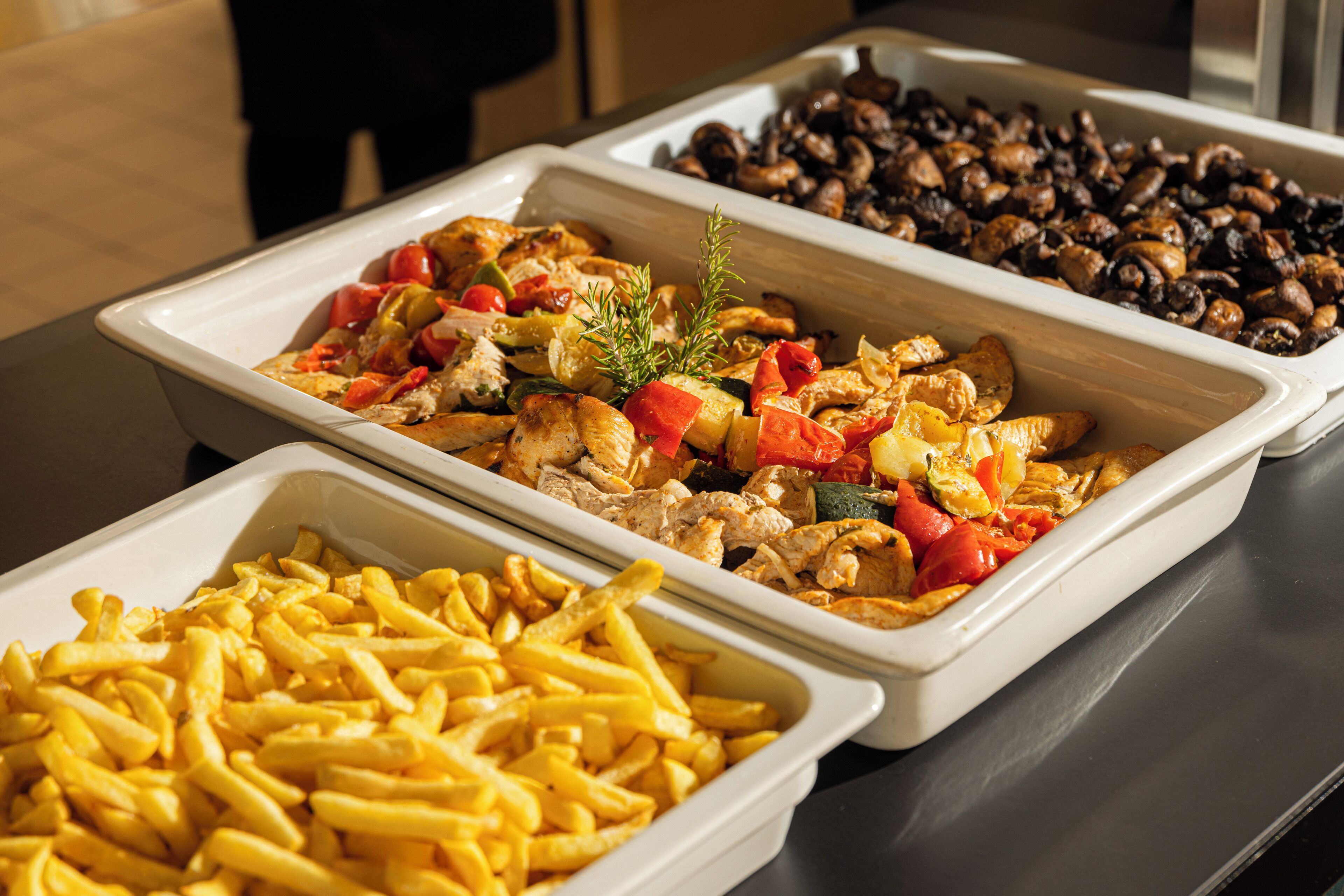 Een buffet met drie schalen eten: frieten, een gerecht met kip en groenten, en een paddenstoelen gerecht.