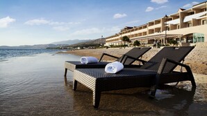 Um hotel à beira-mar com espreguiçadeiras e toalhas na areia, com vista para o mar e as montanhas.