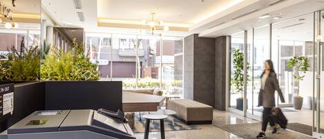 A modern lobby with a reception desk, seating area, and large windows offering views of the city.