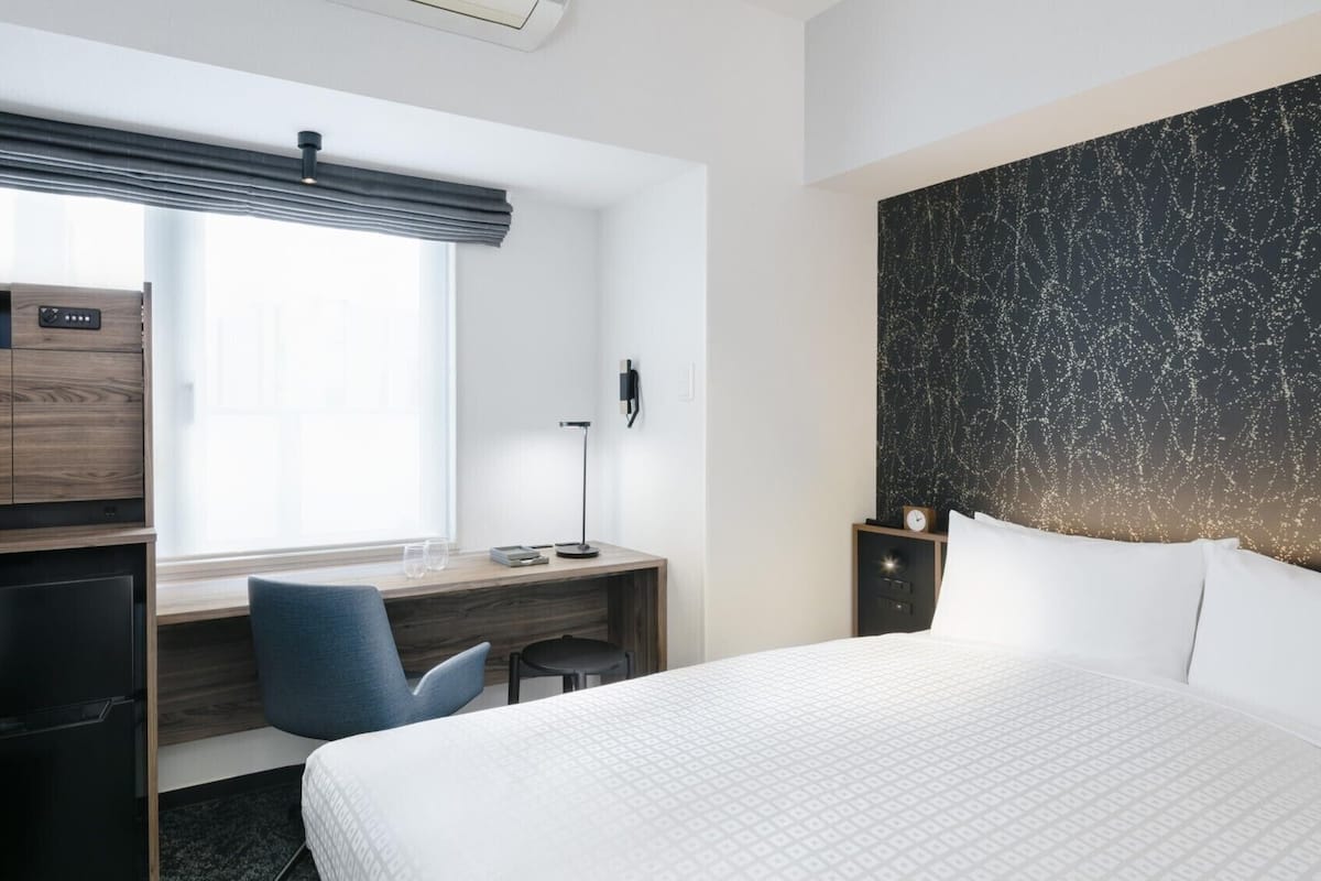 Een hotelkamer met een bed, bureau, stoel en een kledingkast.