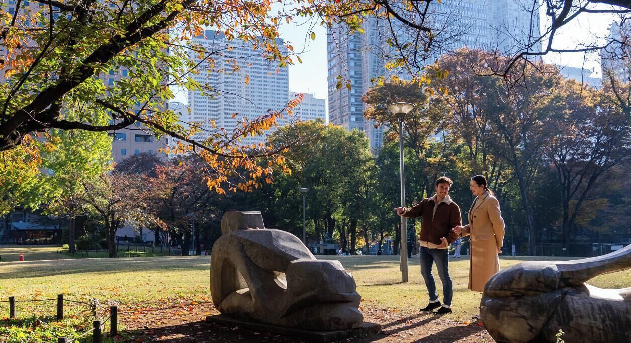 A park with stone sculptures, trees, and a cityscape in the background.