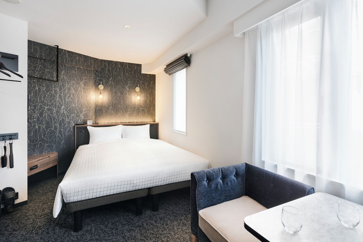 Een moderne hotelkamer met een groot bed, een zithoek met een tafel, en een raam met dunne gordijnen.