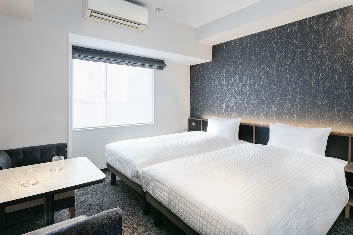 Een hotelkamer met twee bedden, een raam, een tafel en een bank.