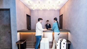 A reception area with a reception desk, a counter, and a seating bench. There are two suitcases and a handbag on the floor.