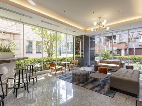 A modern lounge area with a sofa, ottoman, chairs, and a small table. Large windows provide views of the outside.