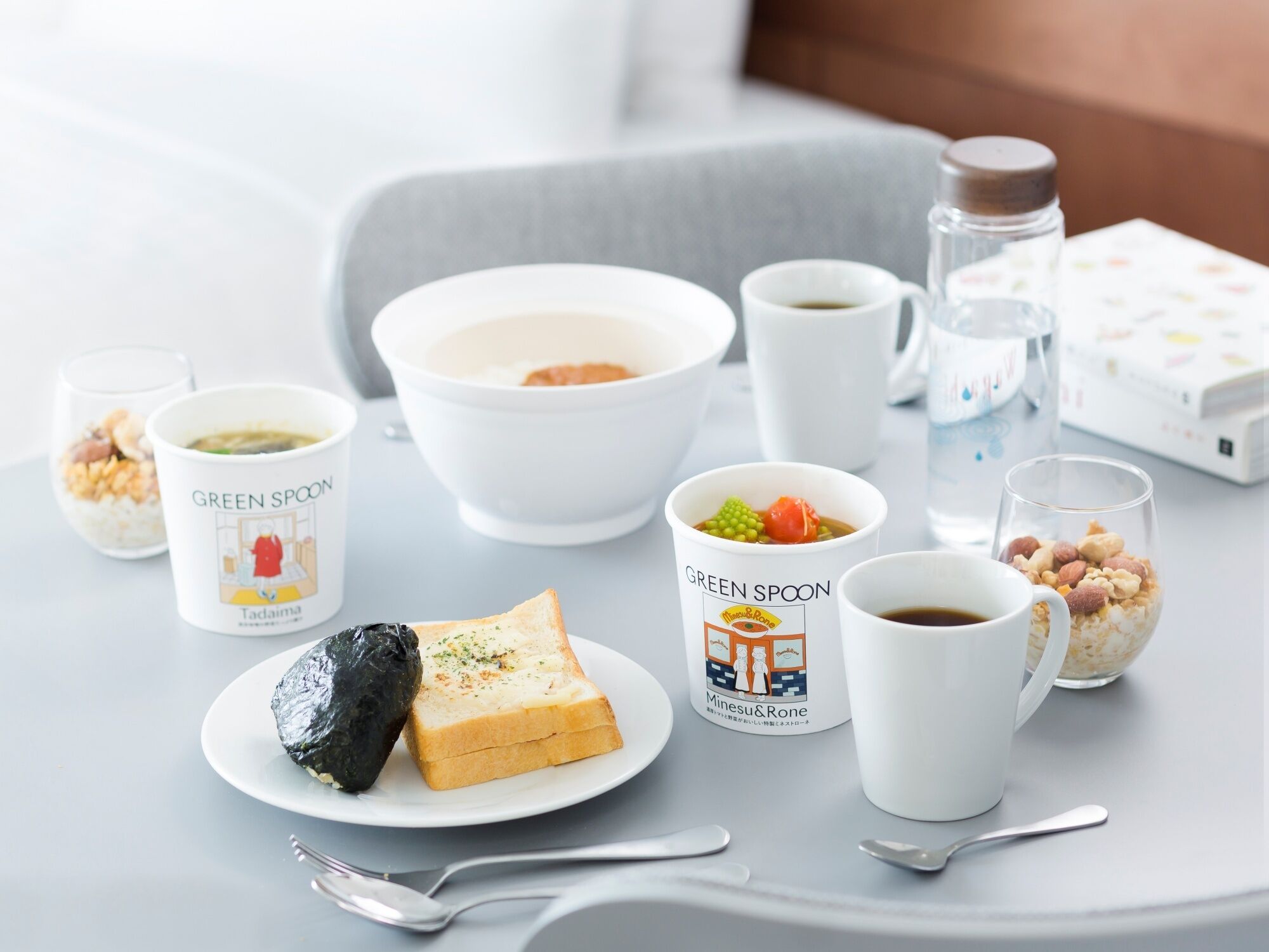 A table set with various food items and drinks, including a bowl of soup, a plate with a sandwich and a wrapped item, and several cups and glasses.