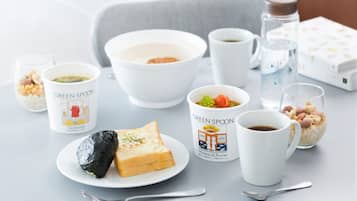 A table set with various food items and drinks, including a bowl of soup, a plate with a sandwich and a wrapped item, and several cups and glasses.