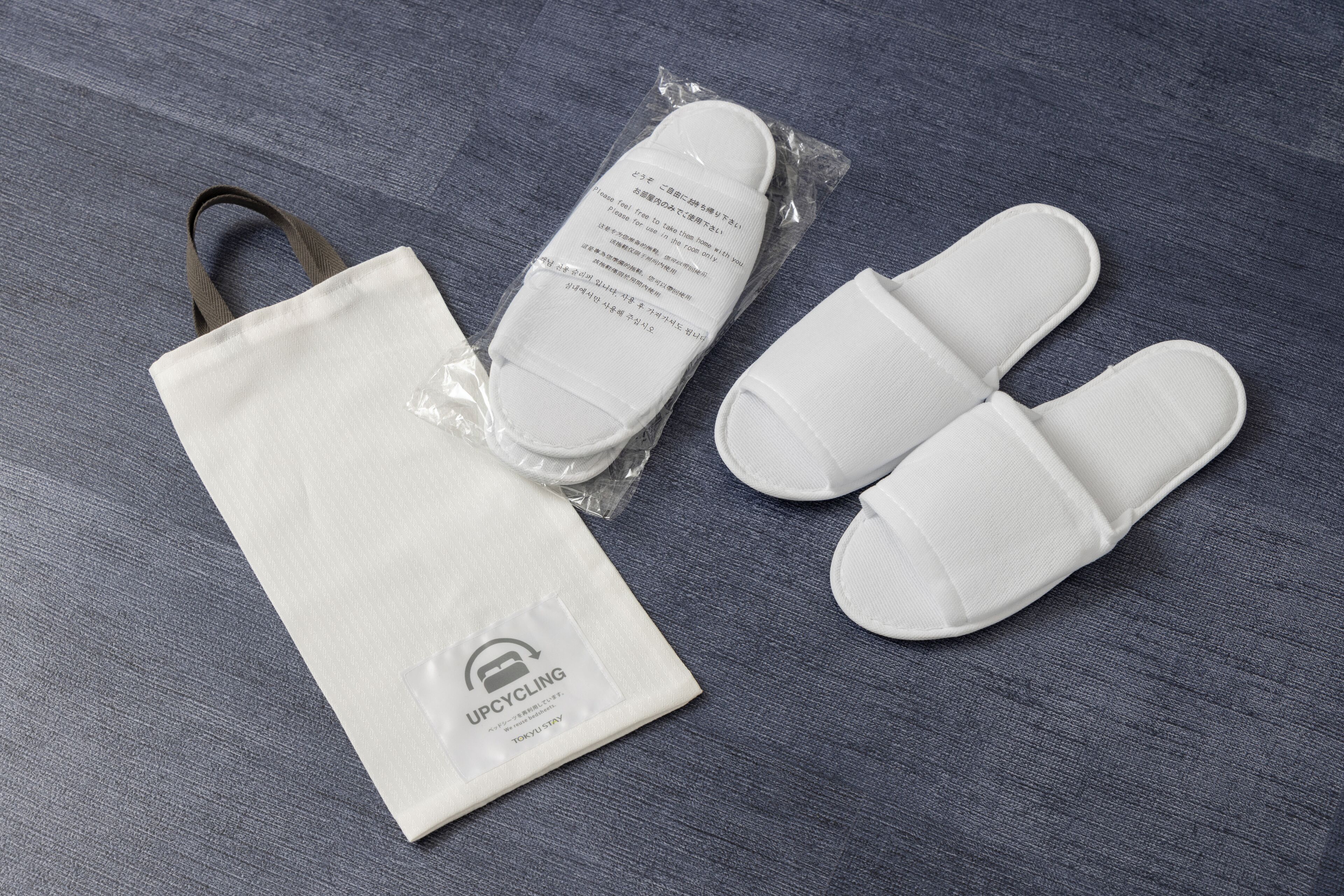 A white reusable bag and a pair of white reusable slippers with a recycling logo.