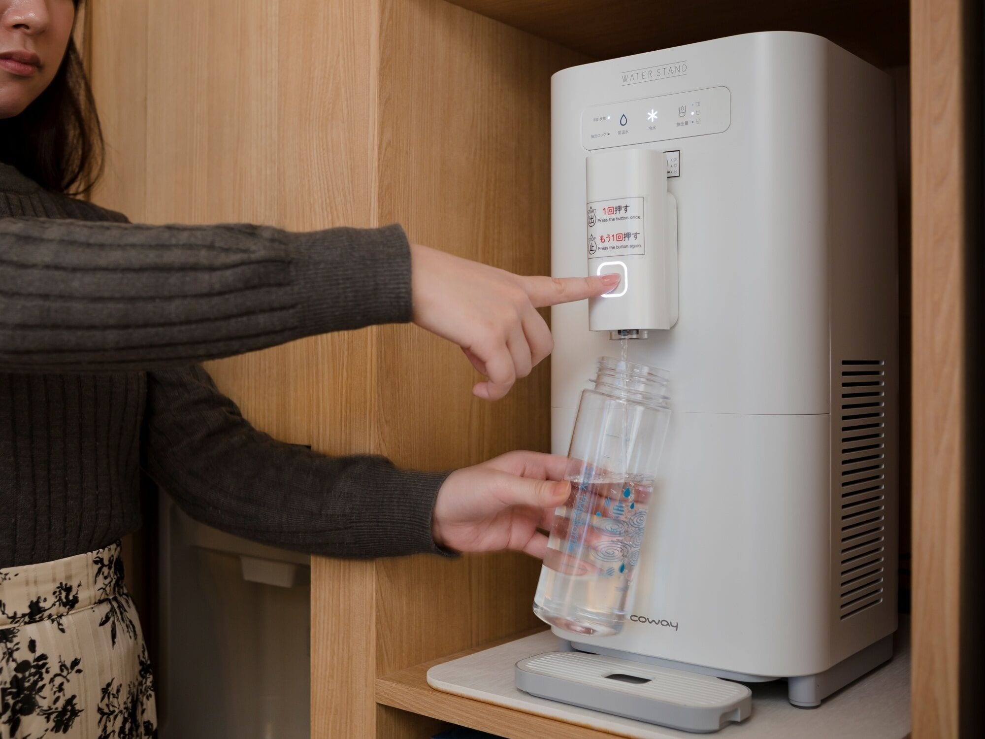 A person using a water dispenser with instructions in multiple languages.