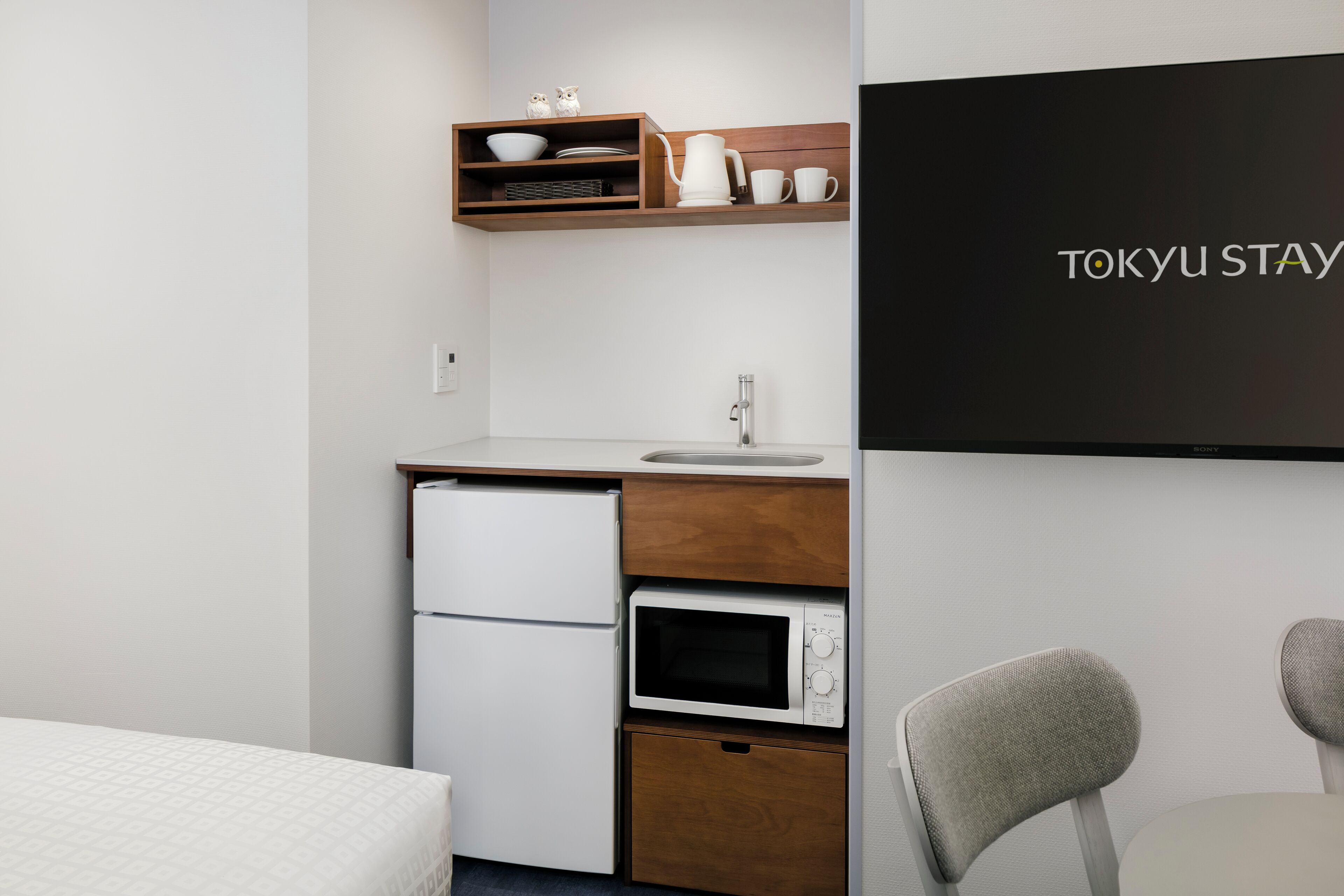 A compact kitchenette with a microwave, refrigerator, and wooden shelf above.