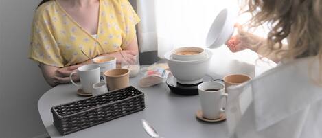 A breakfast setting with a coffee maker, cups, and a basket on a table.