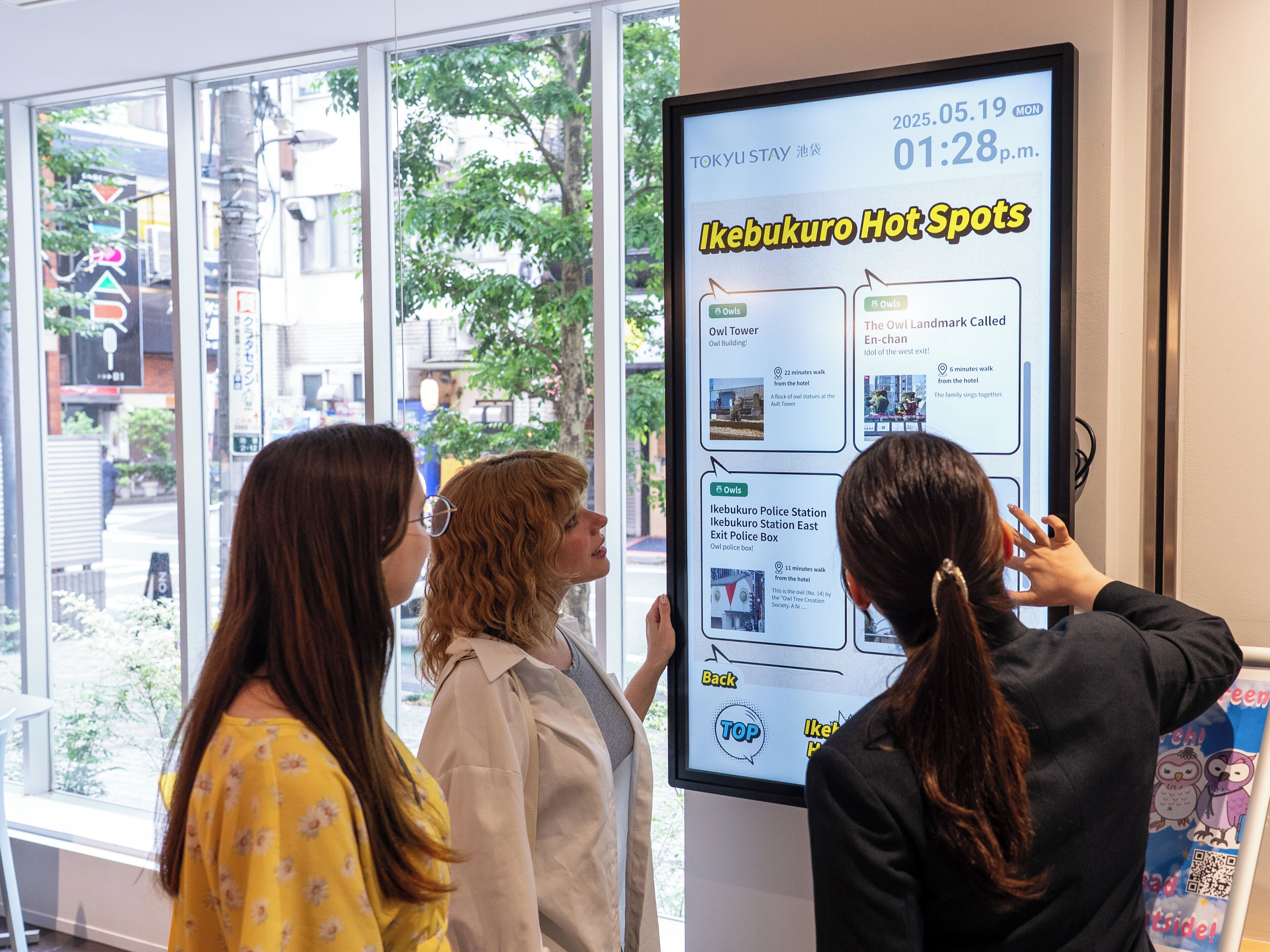 Pantalla digital que muestra 'Ikebukuro Hot Spots' con información sobre tiempos de caminata y ubicaciones como 'Owl Tower' y 'Estación de Policía de Ikebukuro'.