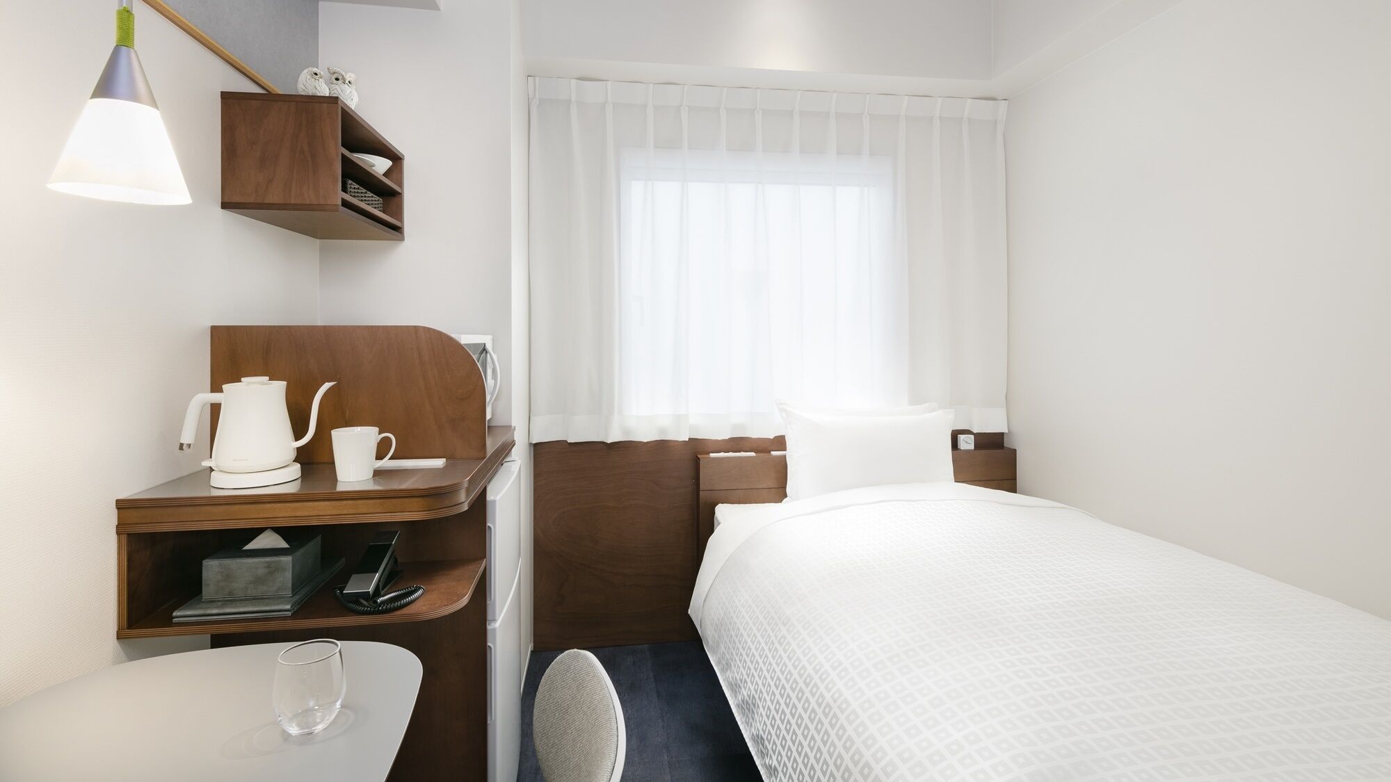 Habitació d'hotel amb un llit, un escriptori amb una paperera, una tassa i un telèfon.