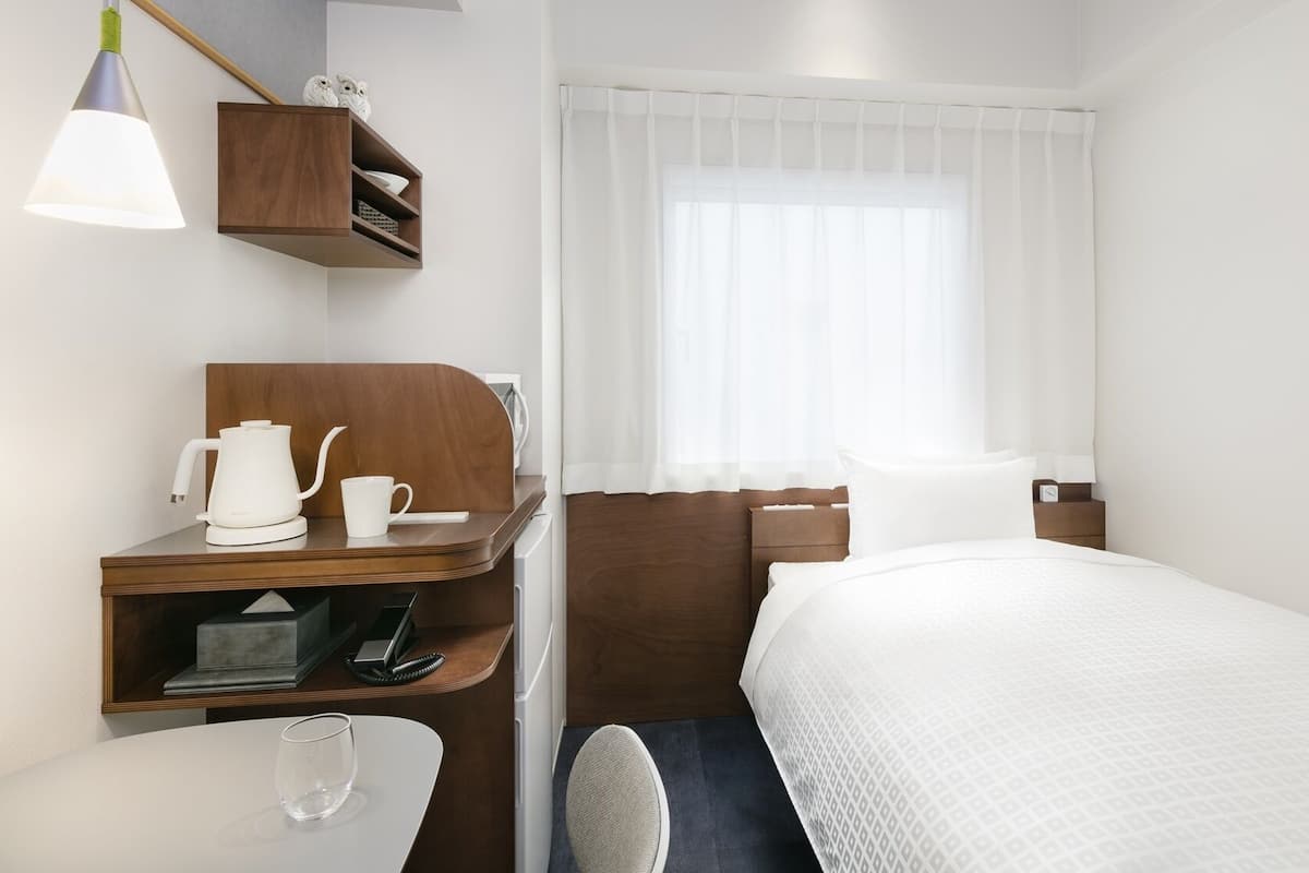 Habitació d'hotel amb un llit, un escriptori amb una paperera, una tassa i un telèfon.